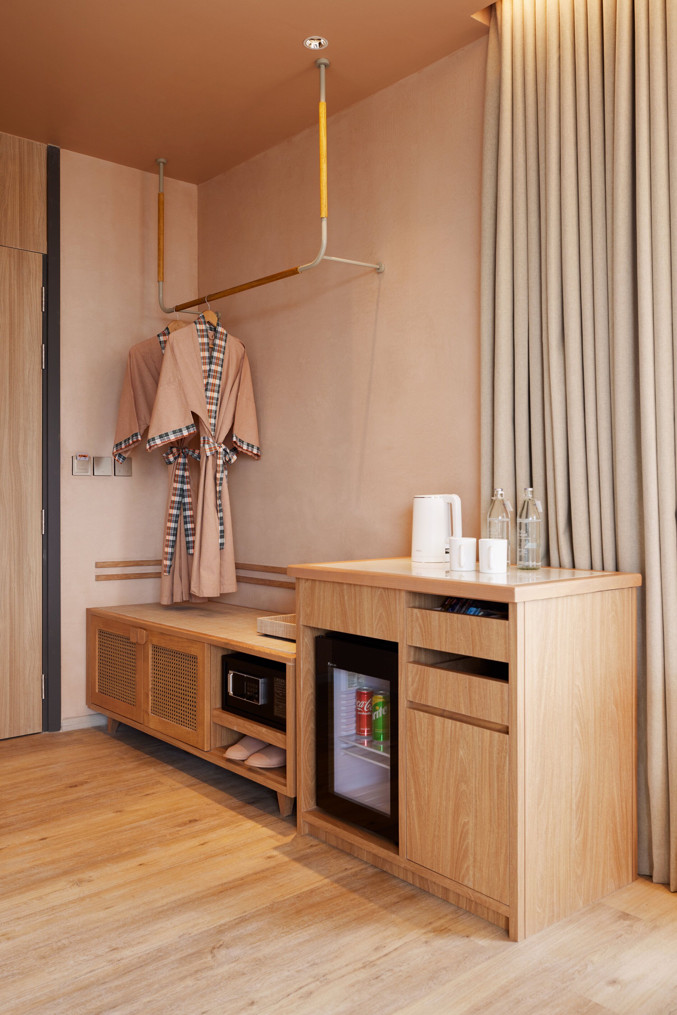 A modern bathroom with a wooden vanity, a robe hanging on a rack, a microwave, and a small refrigerator.