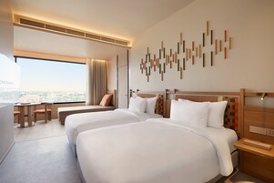Habitación de hotel con dos camas, un escritorio y vistas a la ciudad.