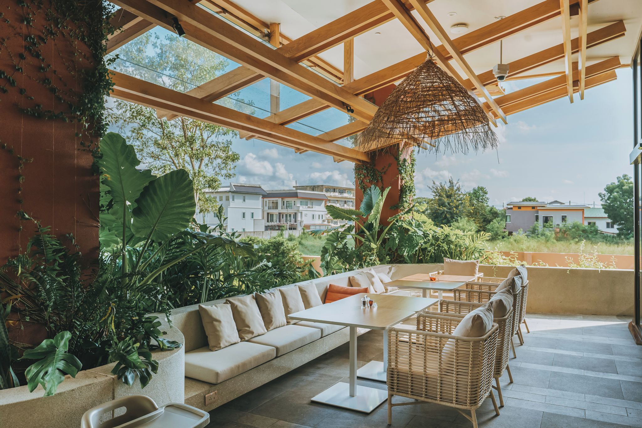 An outdoor seating area with a wooden ceiling, large windows, and lush greenery.