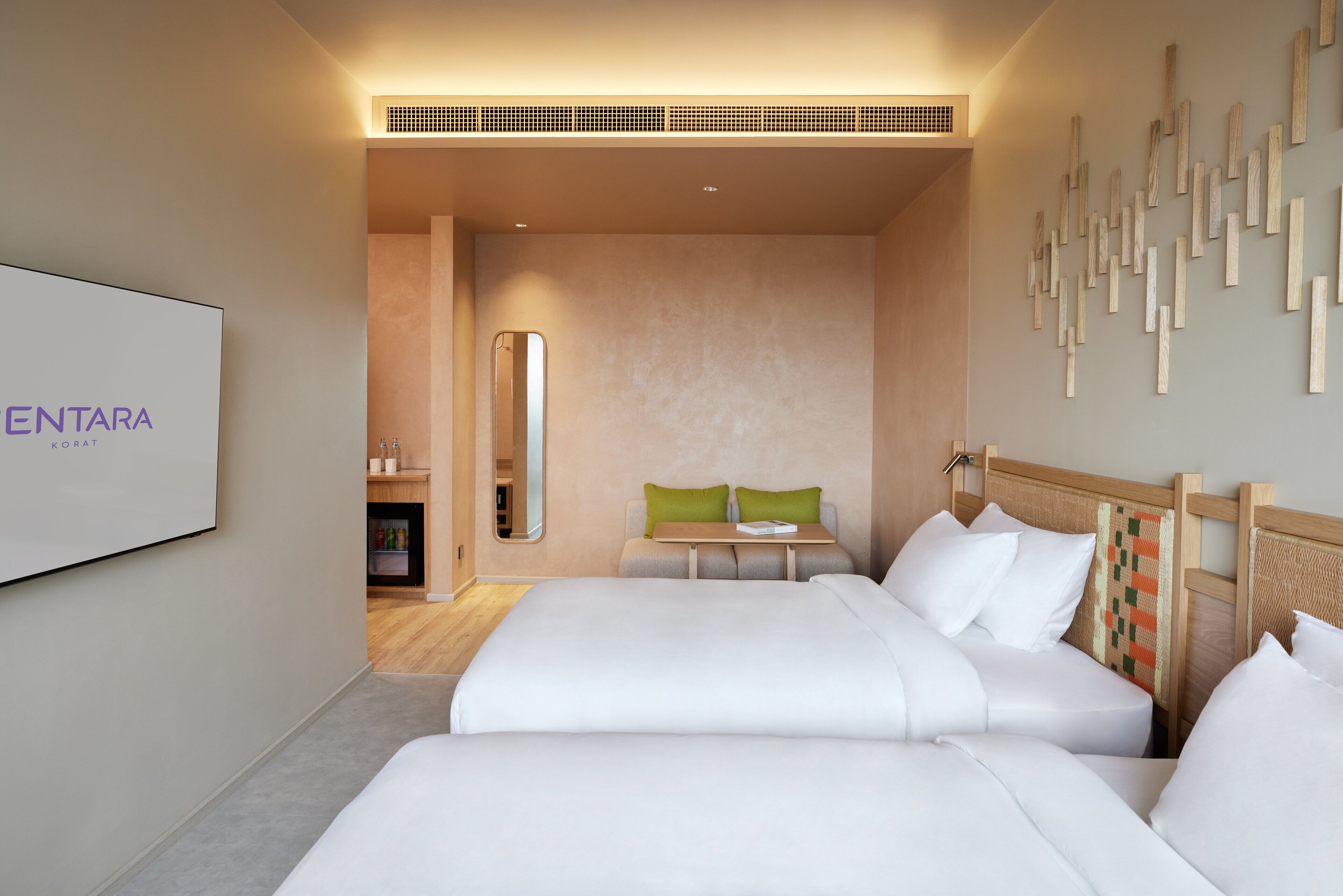 A hotel room with two beds, a small table, a mirror, and a wall-mounted artwork.