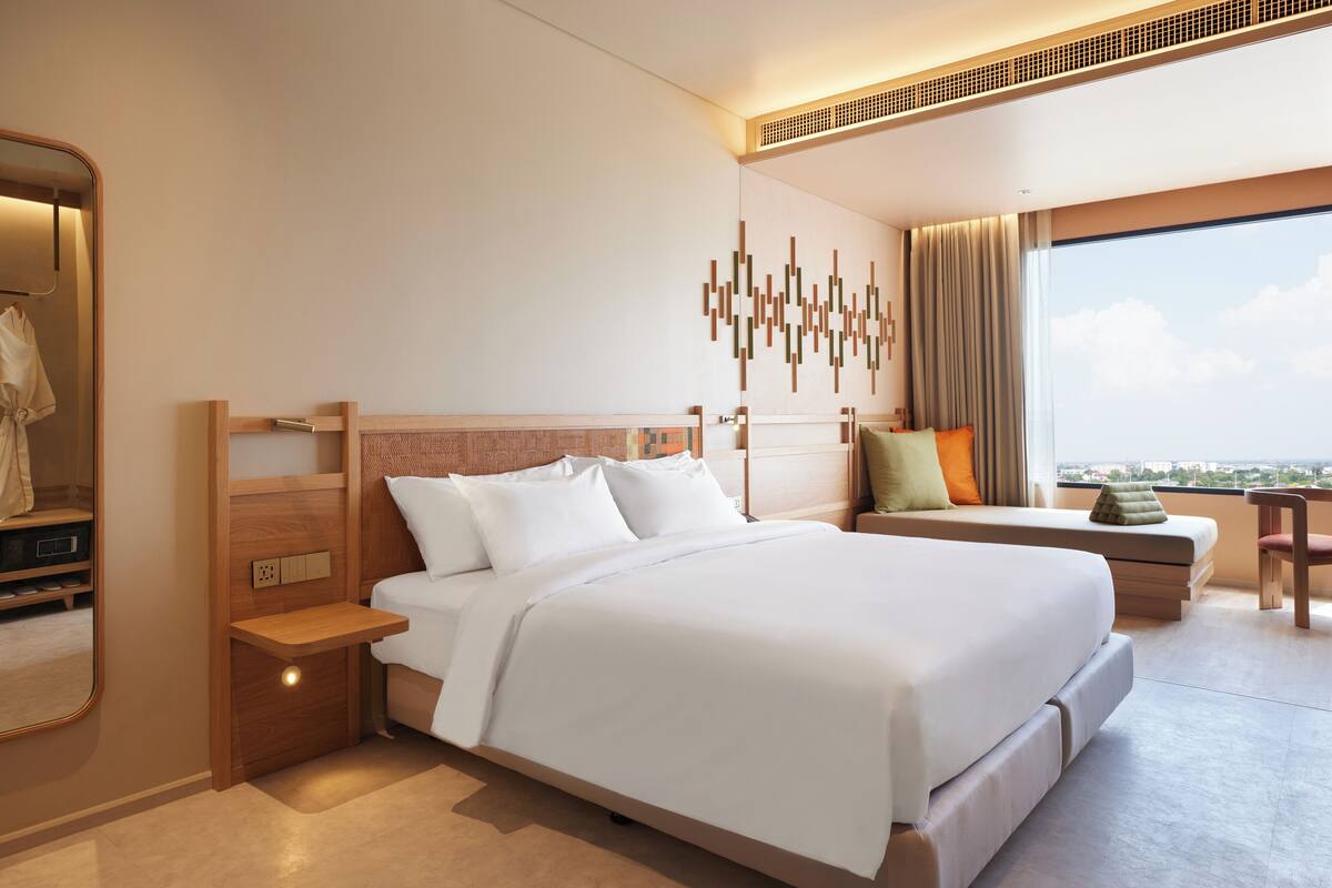 Quarto de hotel moderno com uma cama grande, área de estar, guarda-roupa e vista para a cidade.