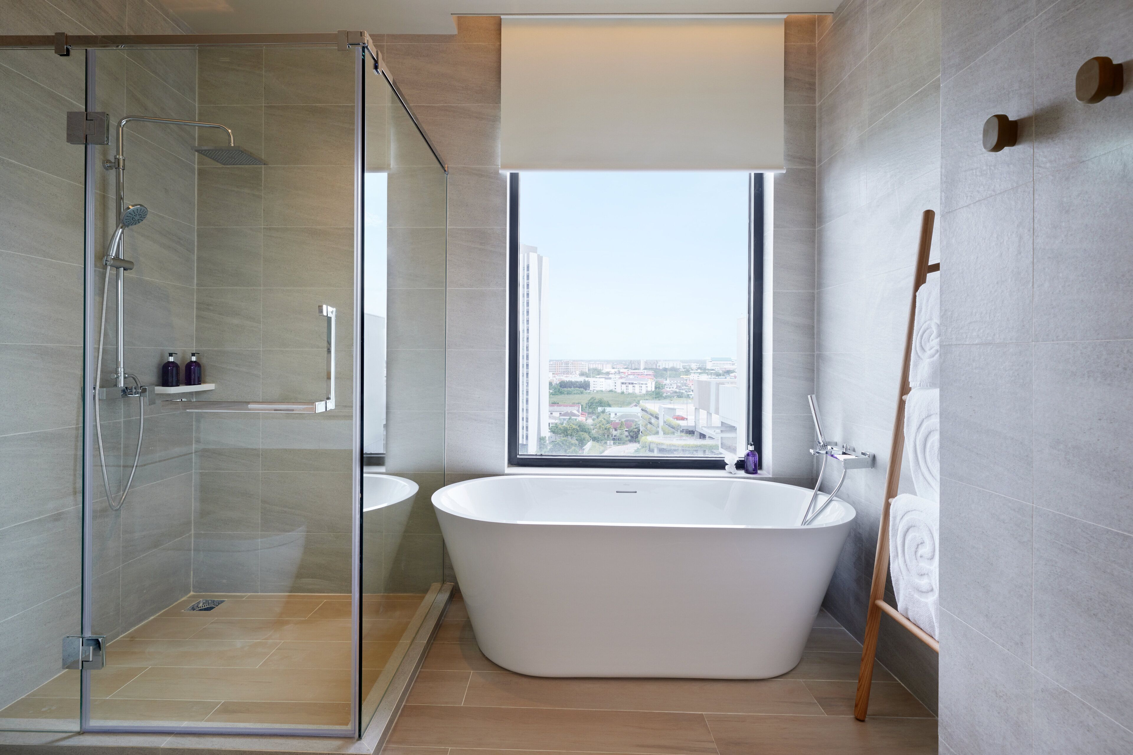 A modern bathroom with a glass-enclosed shower, a freestanding bathtub, and a large window offering a city view.