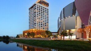 A high-rise hotel with multiple floors, a modern building adjacent to it, and a body of water reflecting the buildings. - Centara Korat (Nakhon Ratchasima)