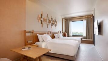 A hotel room with two beds, a wooden desk, a TV, and a large window with curtains.
