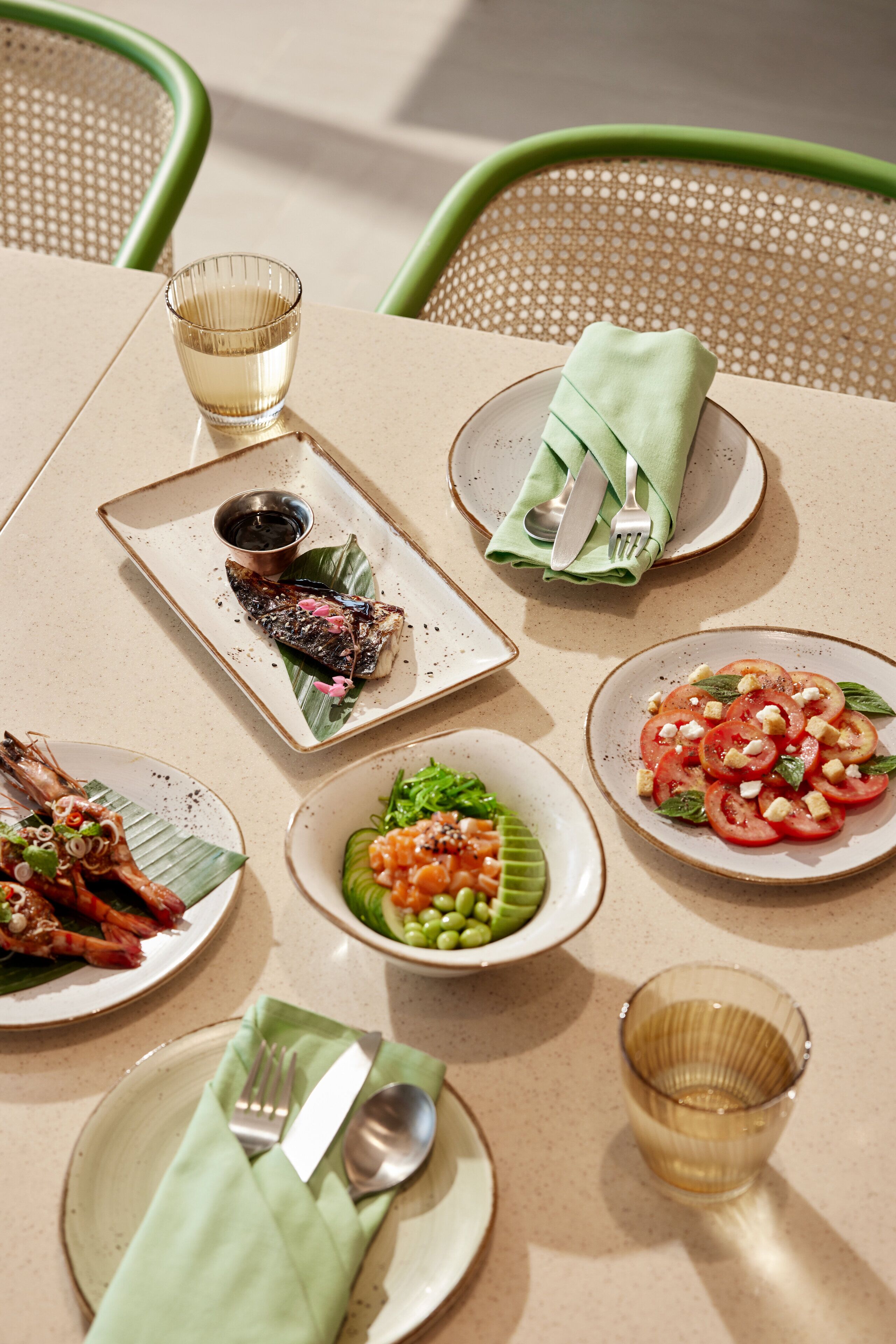 A table set with various dishes, including seafood and salads, arranged on a beige tablecloth.