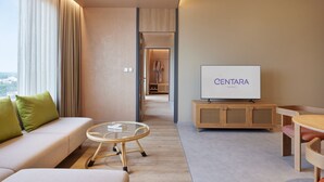 A modern hotel room with a sofa, a glass coffee table, a wooden TV stand, and a view through an open door. - Centara Korat (Nakhon Ratchasima)