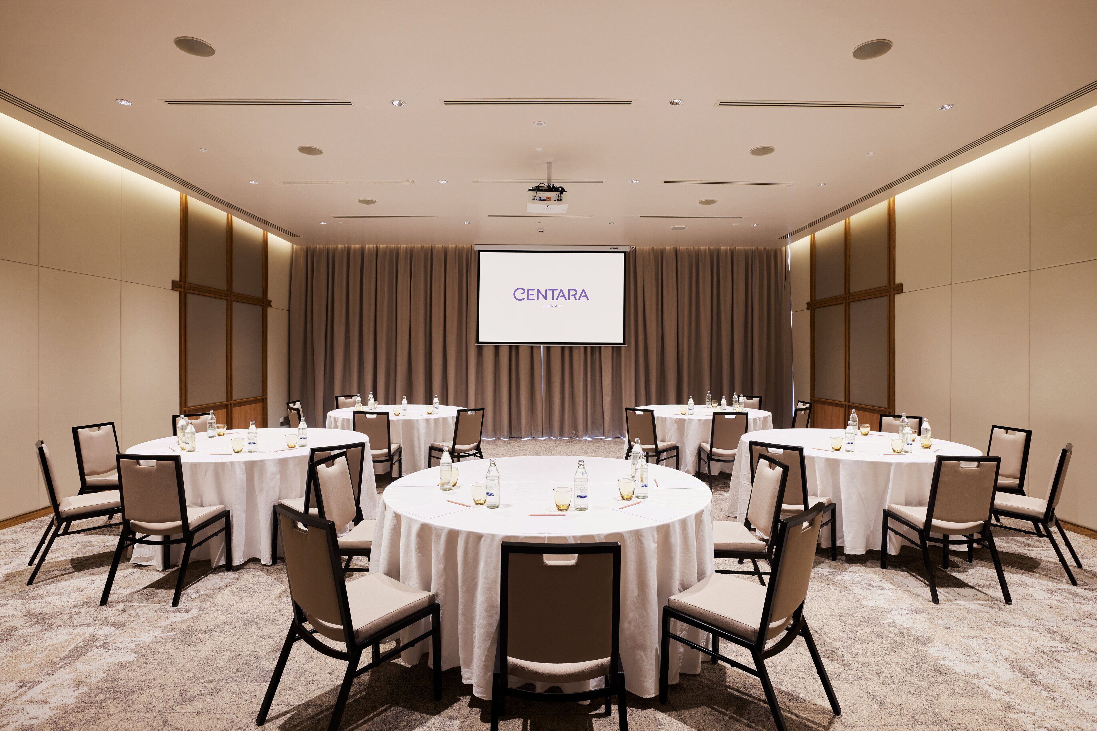 A conference room with multiple round tables, each with chairs, and a large screen displaying "CENTARA" at the front.