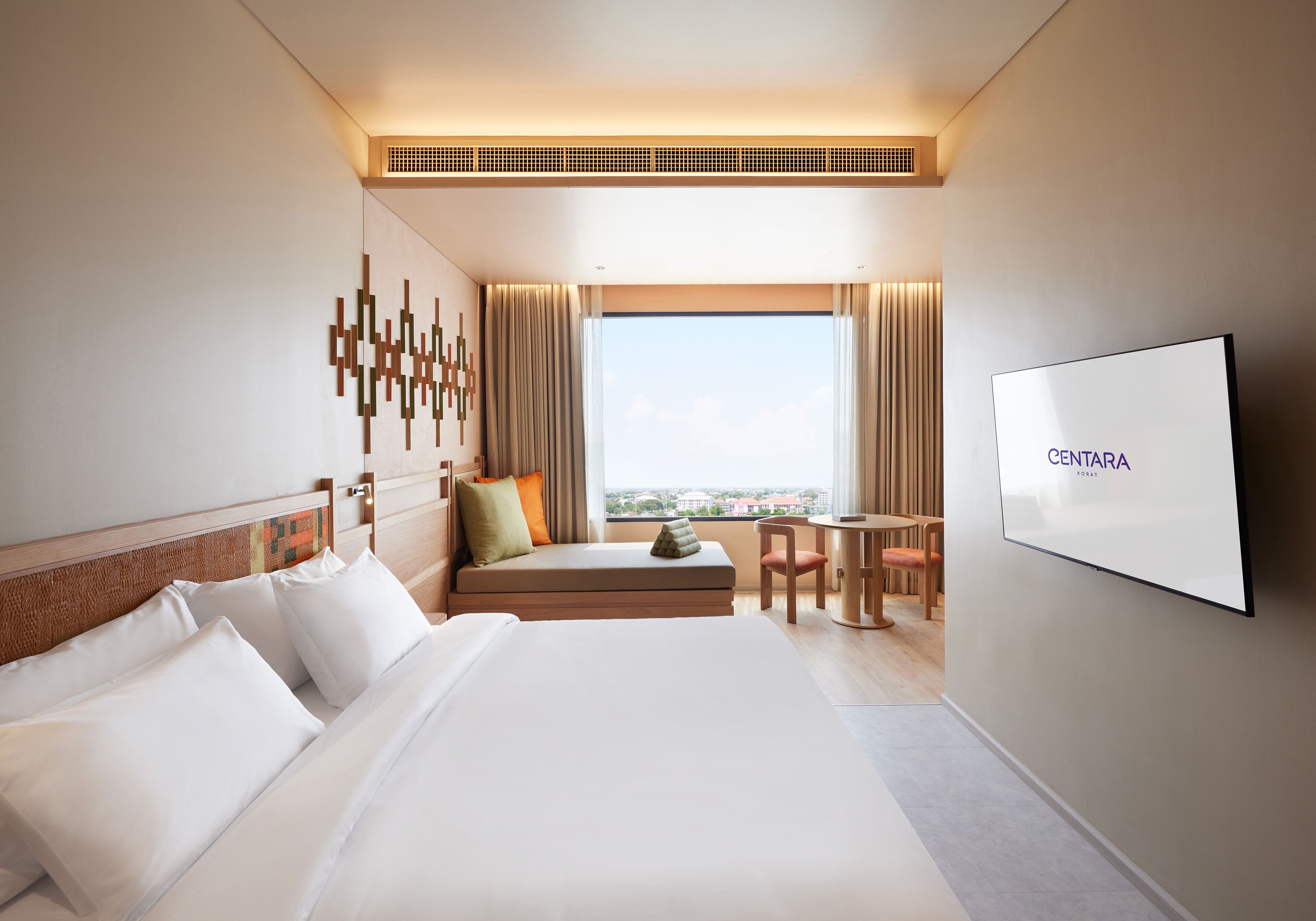 A hotel room with a large bed, a seating area with a view, a TV, and a window with curtains.