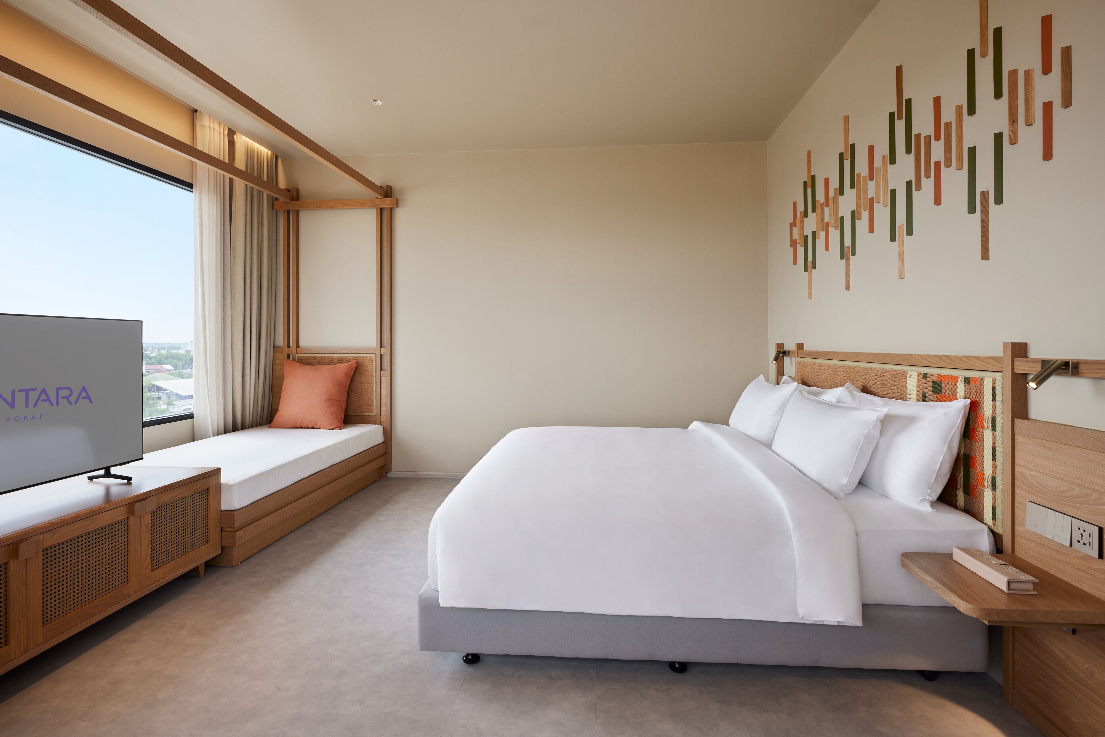 A modern hotel room with a large bed, a TV on a wooden console, a window with curtains, and a wall with a geometric pattern.