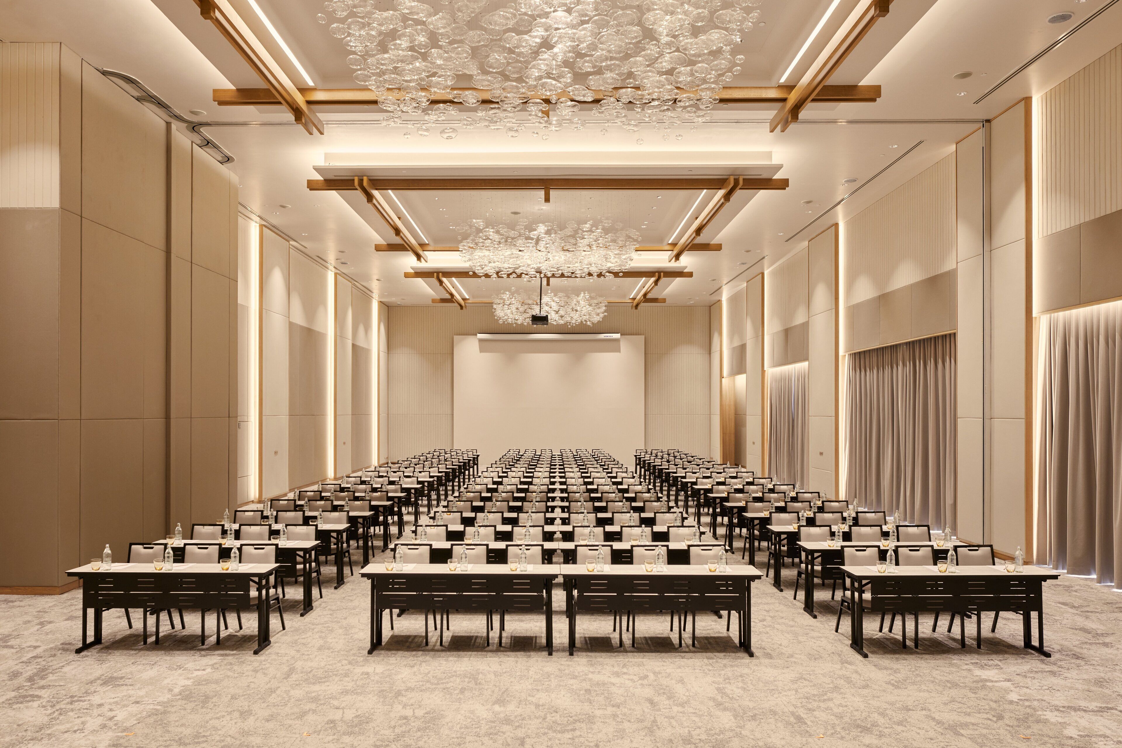 A conference room with rows of tables, a chandelier, and a high ceiling.