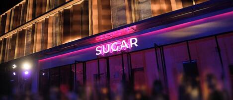 Un bâtiment doté d'une enseigne au néon sur laquelle on peut lire le mot « SUGAR » et présentant un design architectural moderne.