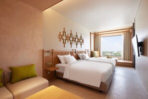 A hotel room with two beds, a sofa, a TV, and a window with a view.