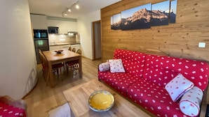 Un salon chaleureux avec un canapé rouge, des murs en bois et un coin repas comprenant une table et des chaises en bois.