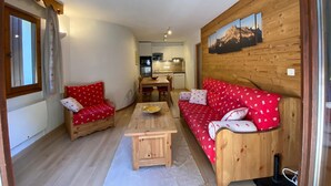 Un salon chaleureux avec deux canapés rouges, une table basse en bois et une cuisine en arrière-plan.
