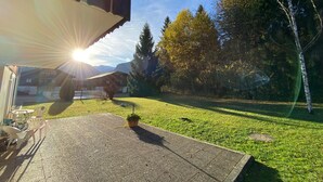 Un espace patio offrant une vue sur une chaîne de montagnes, une pelouse verdoyante et un bâtiment en arrière-plan.