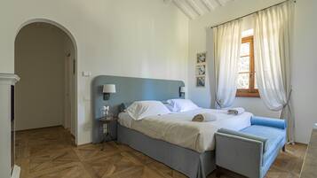A bedroom with a bed, bedside tables, a chair, a window with curtains, and a wooden floor.