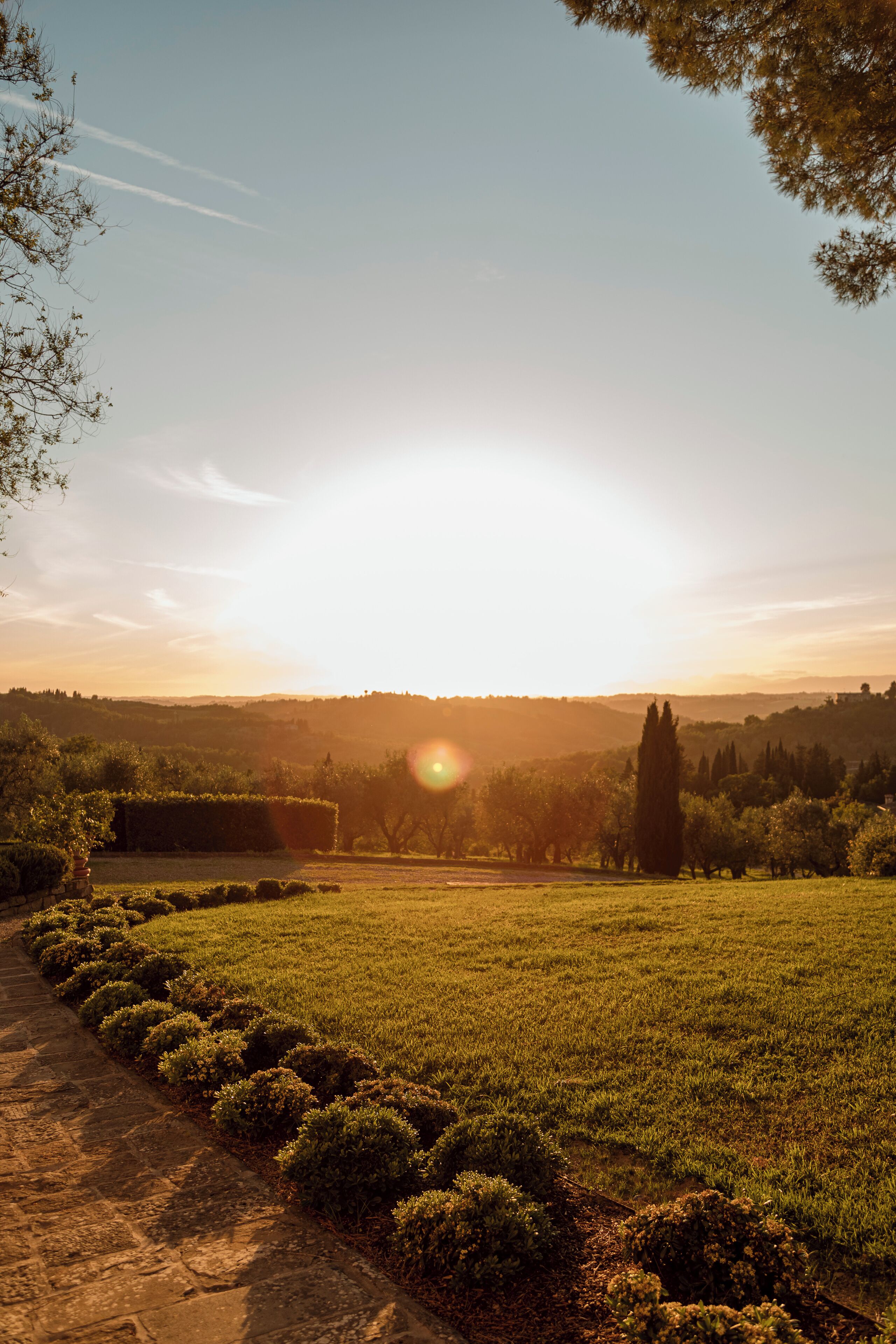 A garden with a stone pathway, neatly trimmed bushes, and a view of distant hills.