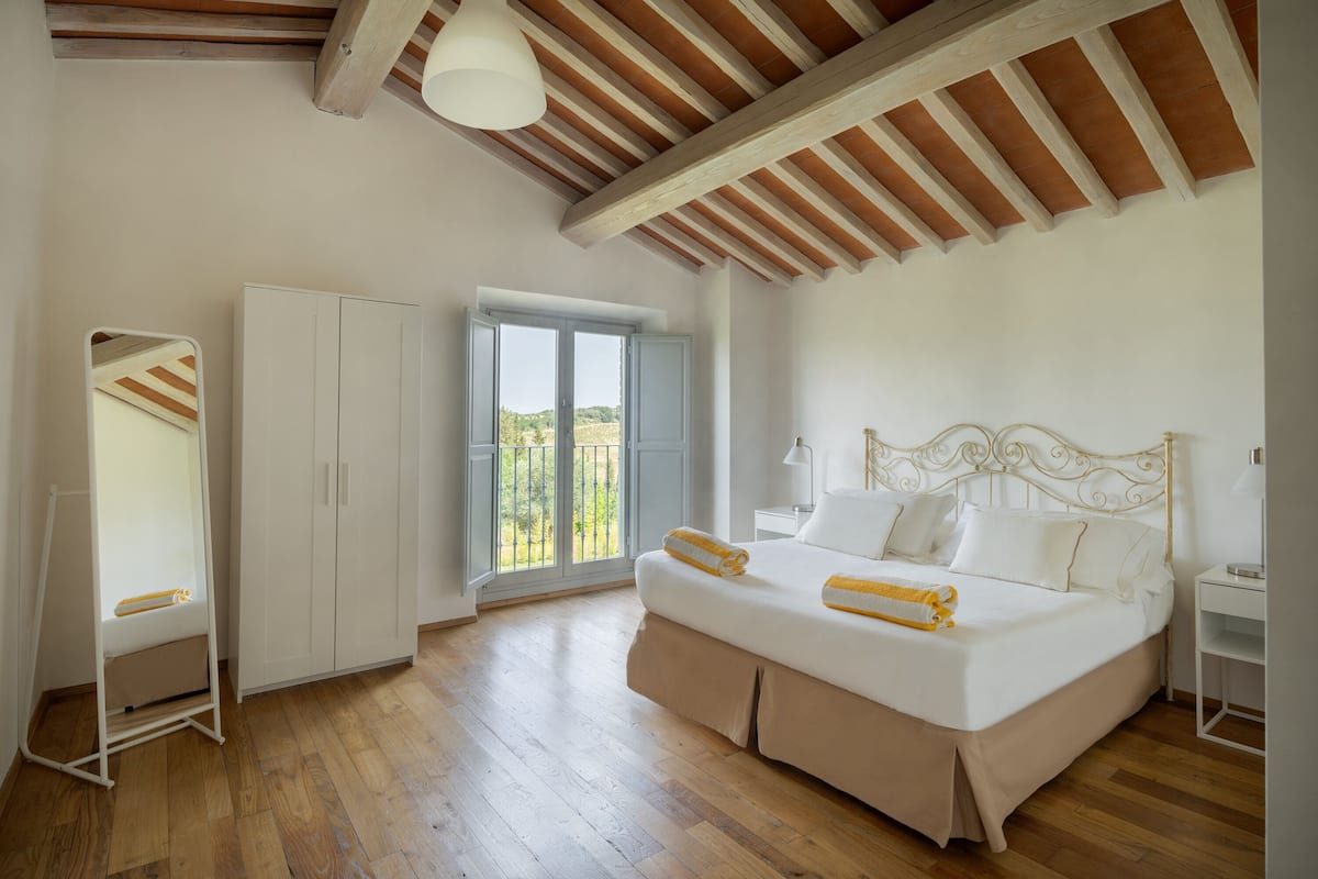 A bedroom with a large bed, wooden flooring, a wardrobe, and a window with a view.