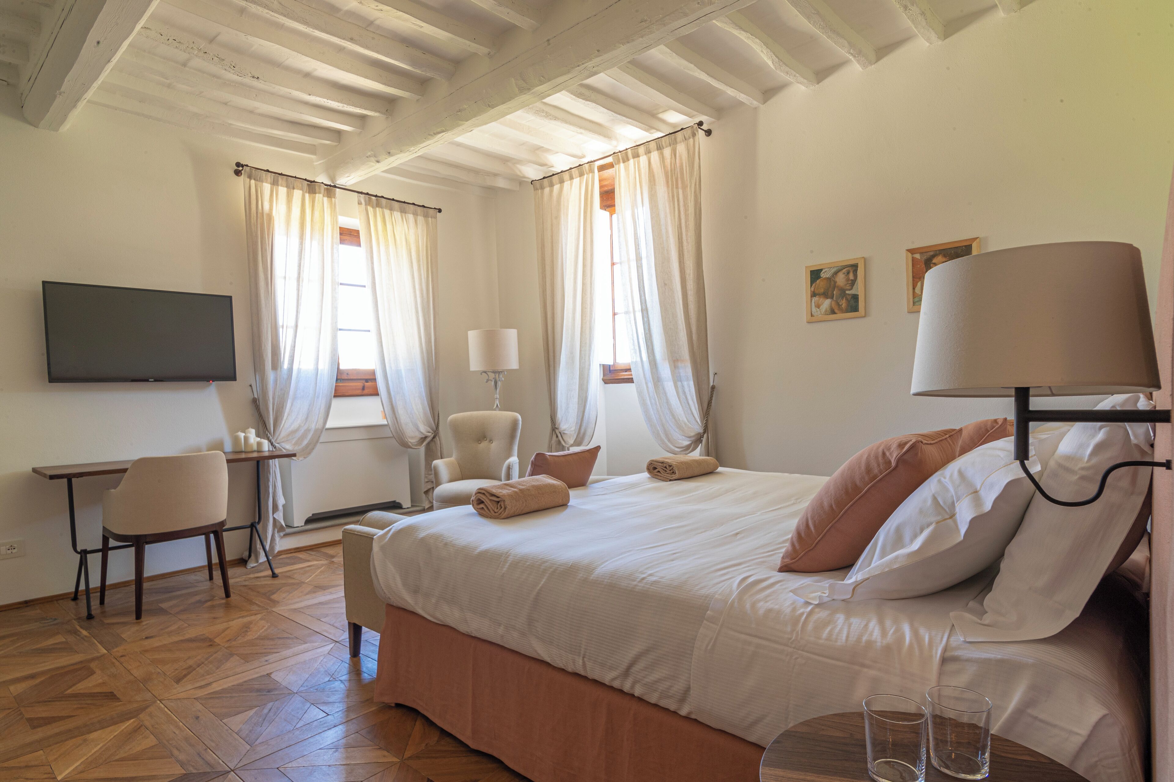 A bedroom with a bed, a desk, a chair, a TV, and curtains.