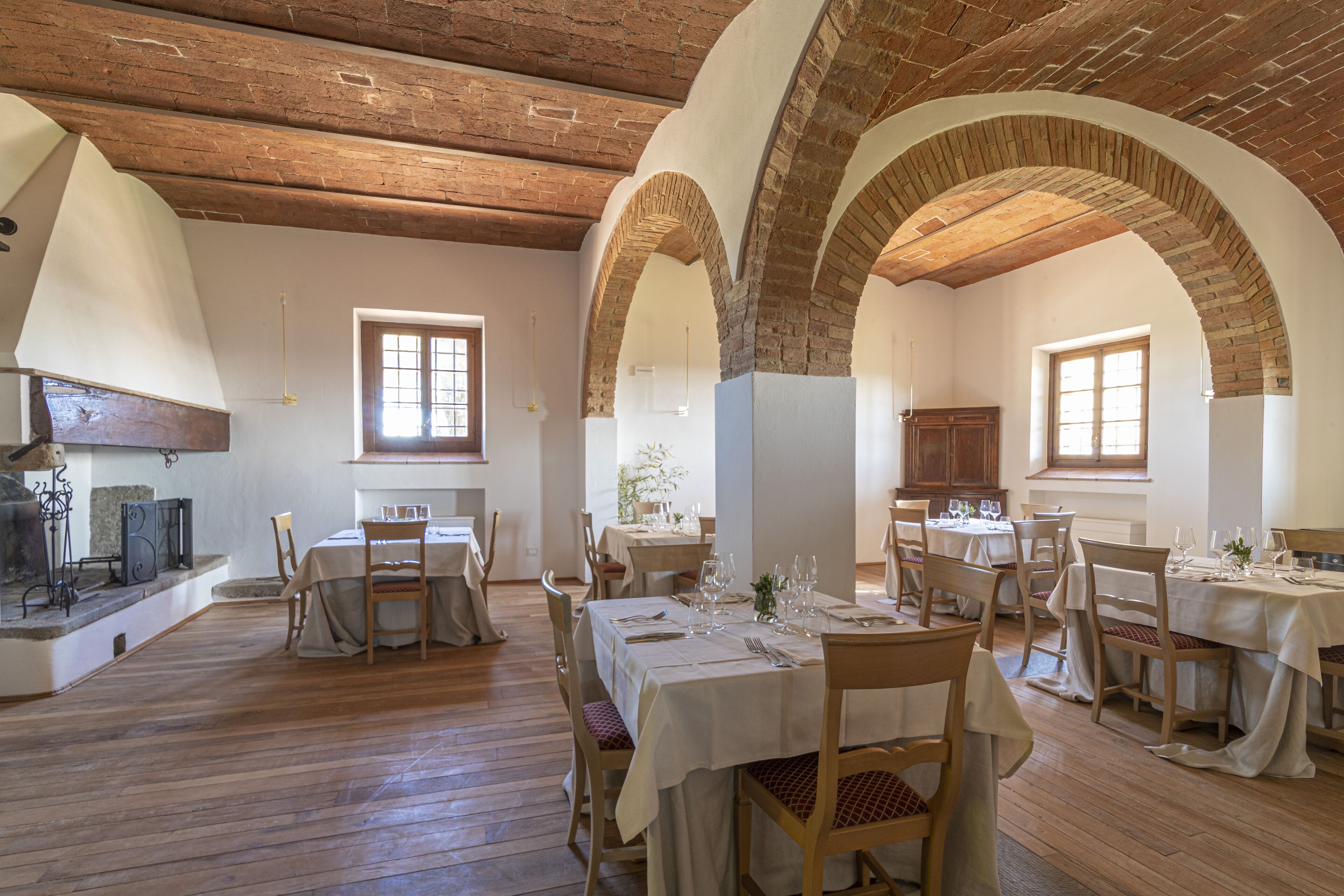 A dining area with multiple tables and chairs, brick arches, and wooden floors.