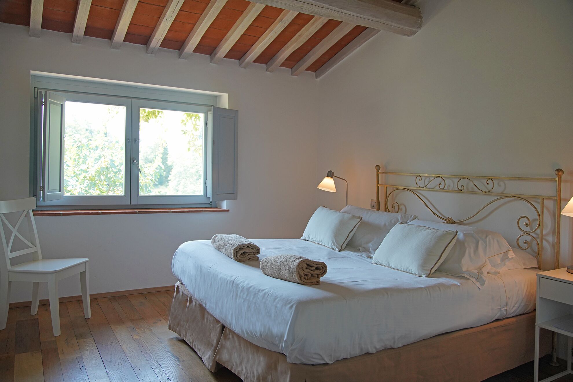 Un dormitorio con cama, una silla, una mesita de noche y un ventanal con vista a árboles.