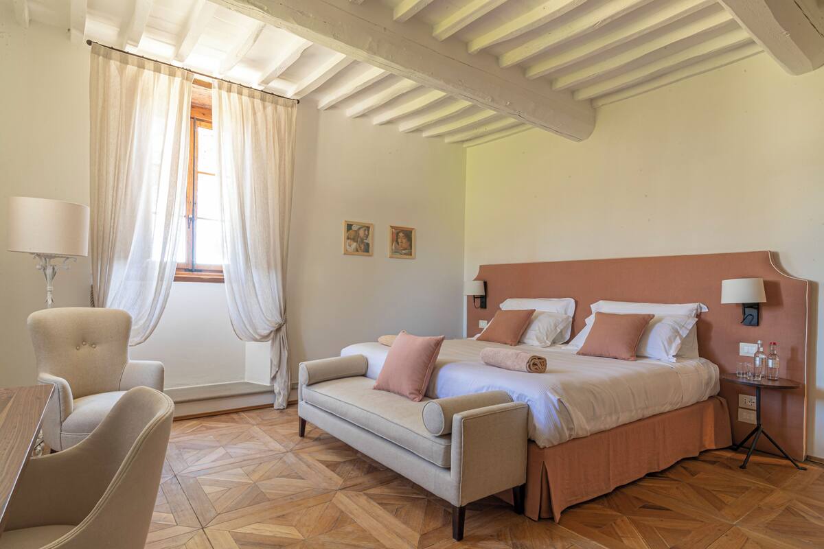 A hotel room with a bed, a sofa, a chair, a nightstand, and a lamp.