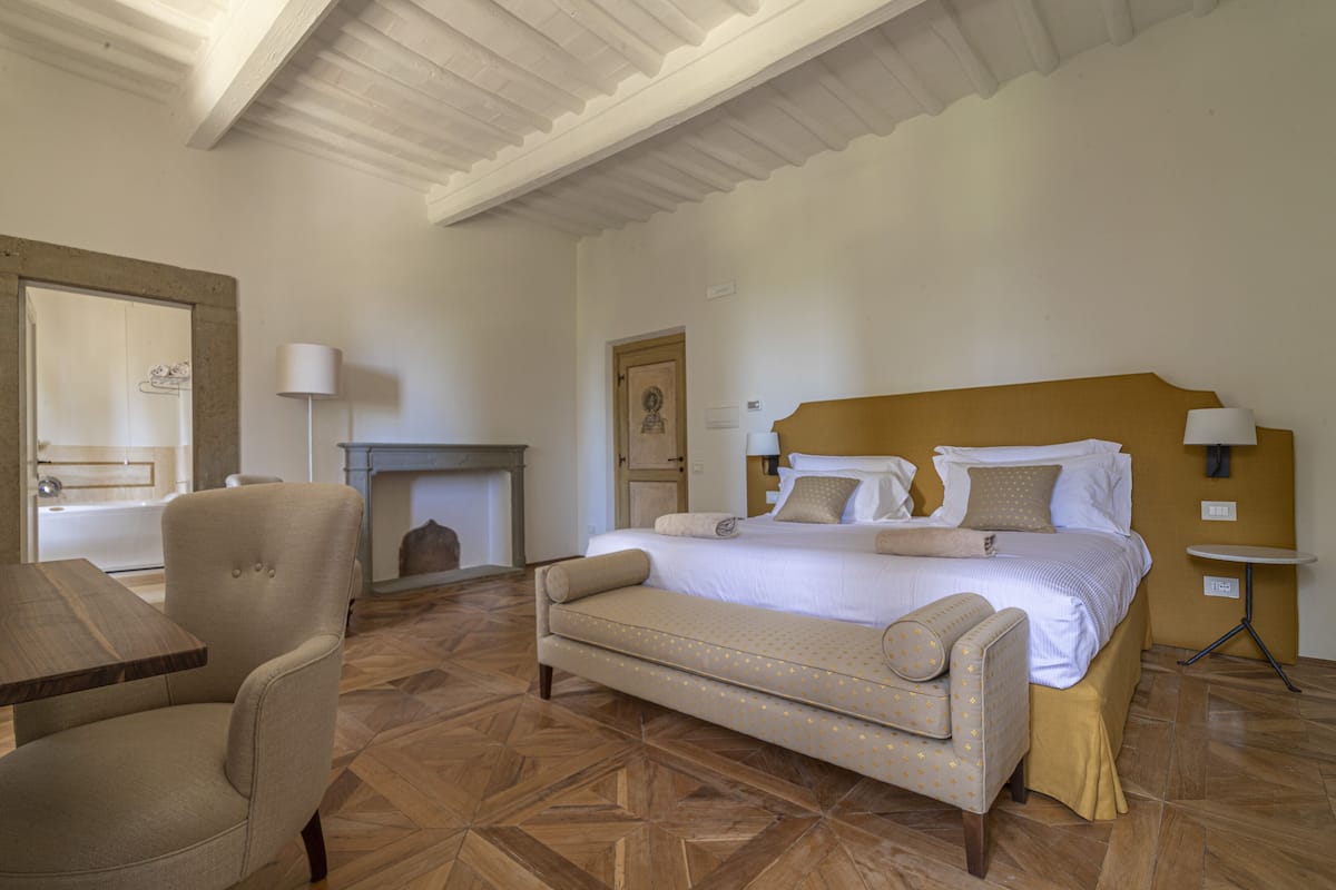 A bedroom with a bed, a chair, a table, and a fireplace.