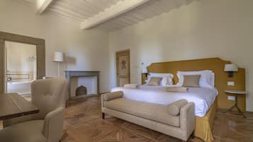 A bedroom with a bed, a chair, a table, and a fireplace.