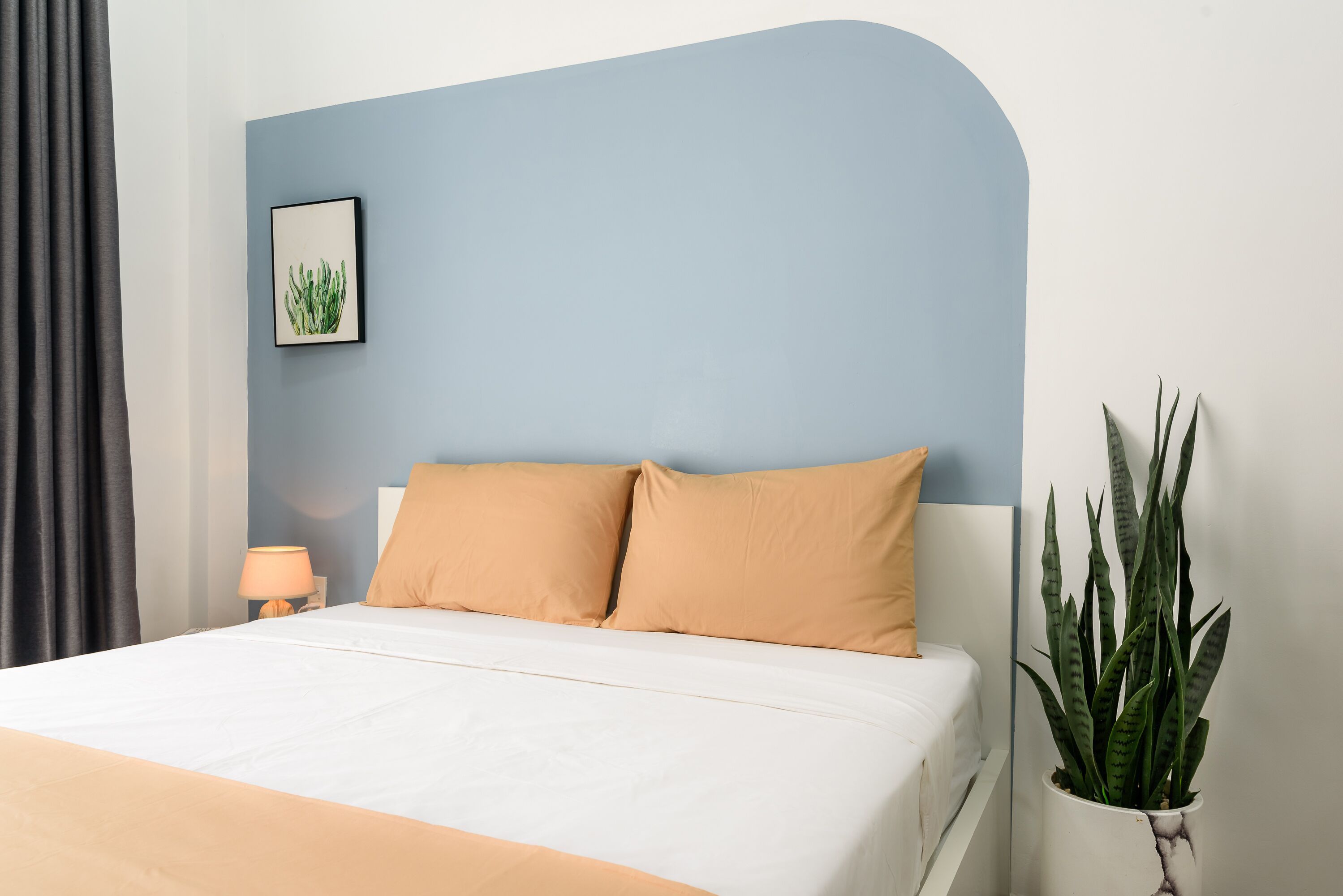 Une chambre à coucher avec un lit, deux oreillers, une lampe de chevet, un tableau encadré et une plante en pot.