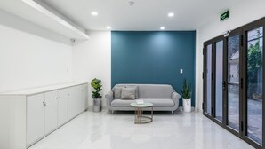 A reception area with a white reception desk, a grey sofa, a small round table, and a potted plant. - Cozrum Homes - Summer's House (Ho Chi Minh City)