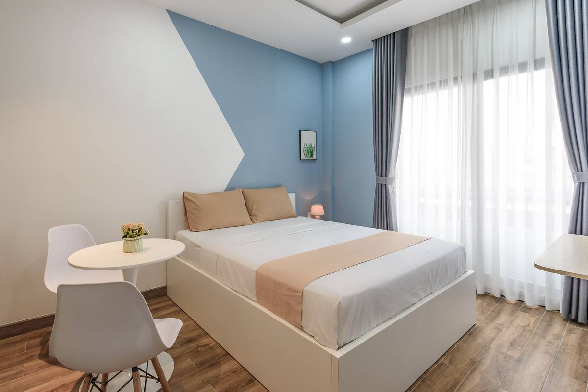 Un dormitorio moderno con una cama, una mesita con un jarrón de flores y una silla.