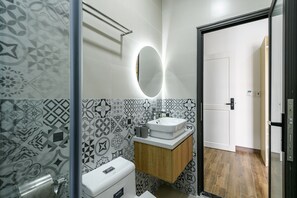 Bathroom features a geometric tile design, a wall-mounted sink, and a round mirror above a wooden vanity.