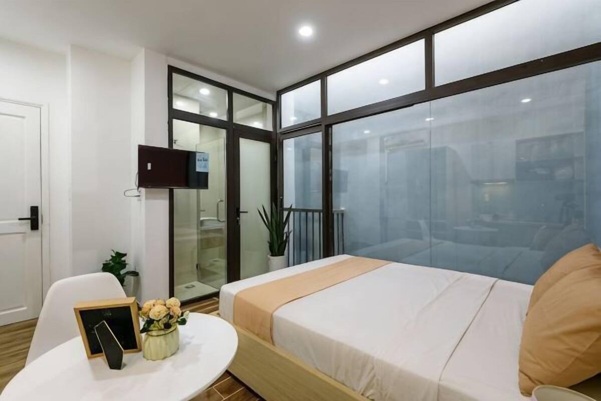 Una habitación de hotel con cama, televisión, escritorio con silla, una mesita con un florero y un balcón con vistas.