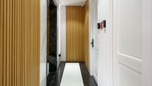 A hallway with a wooden panel wall, a black marble floor, and a white door with a black handle. - Cozrum Homes - Summer's House (Ho Chi Minh City)