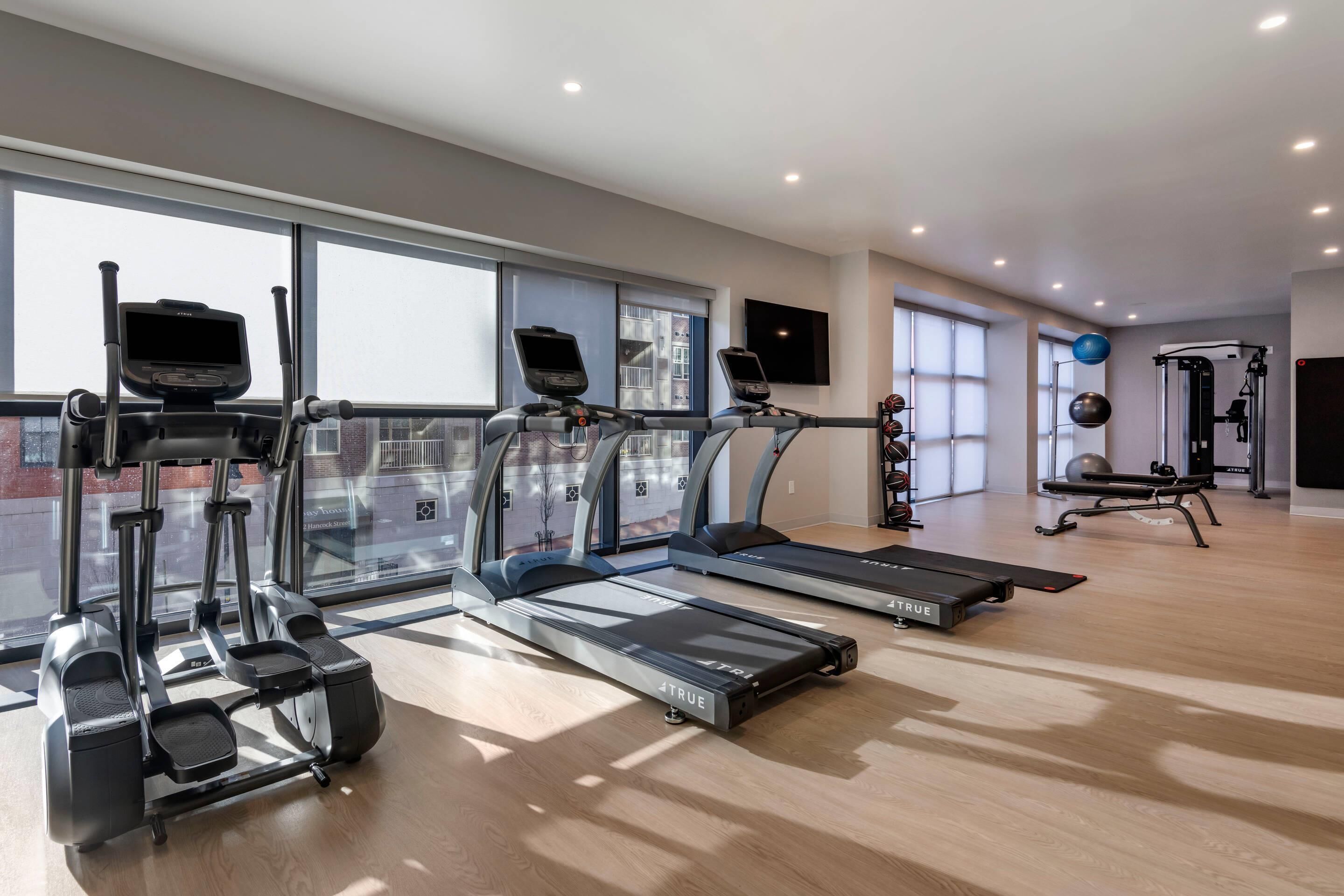 A modern gym with treadmills, elliptical machines, and a rowing machine.