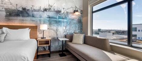 Een moderne hotelkamer met een groot raam, een bed, een slaapbank, een nachtkastje en een muurschildering.