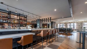 Zona de bar moderna con una barra larga, varios taburetes y una variedad de botellas y vasos en estanterías.