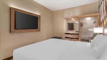 Ein Hotelzimmer mit einem großen Bett, einem an der Wand befestigten Flachbildfernseher, einem Spiegel und einem Nachttisch mit Lampe.