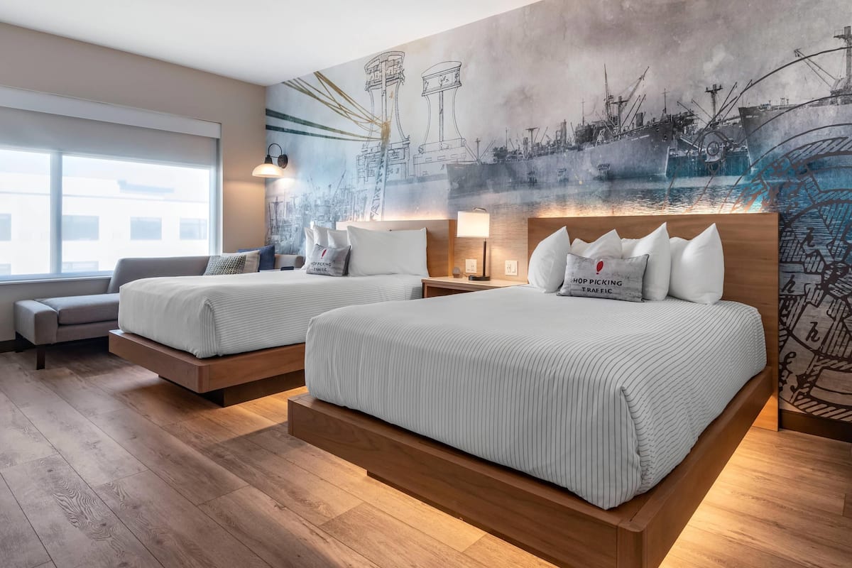 Une chambre d’hôtel moderne avec deux lits, une grande fenêtre et une fresque représentant un paysage portuaire.