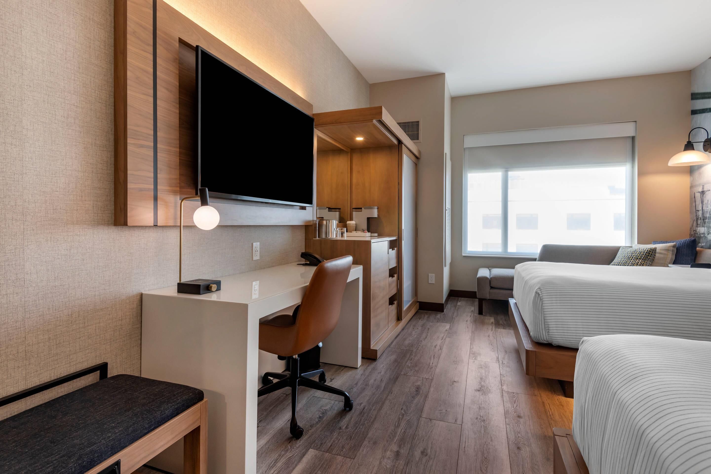 Ein Hotelzimmer mit Bett, Schreibtisch, Sessel, Fernseher und Fenster.