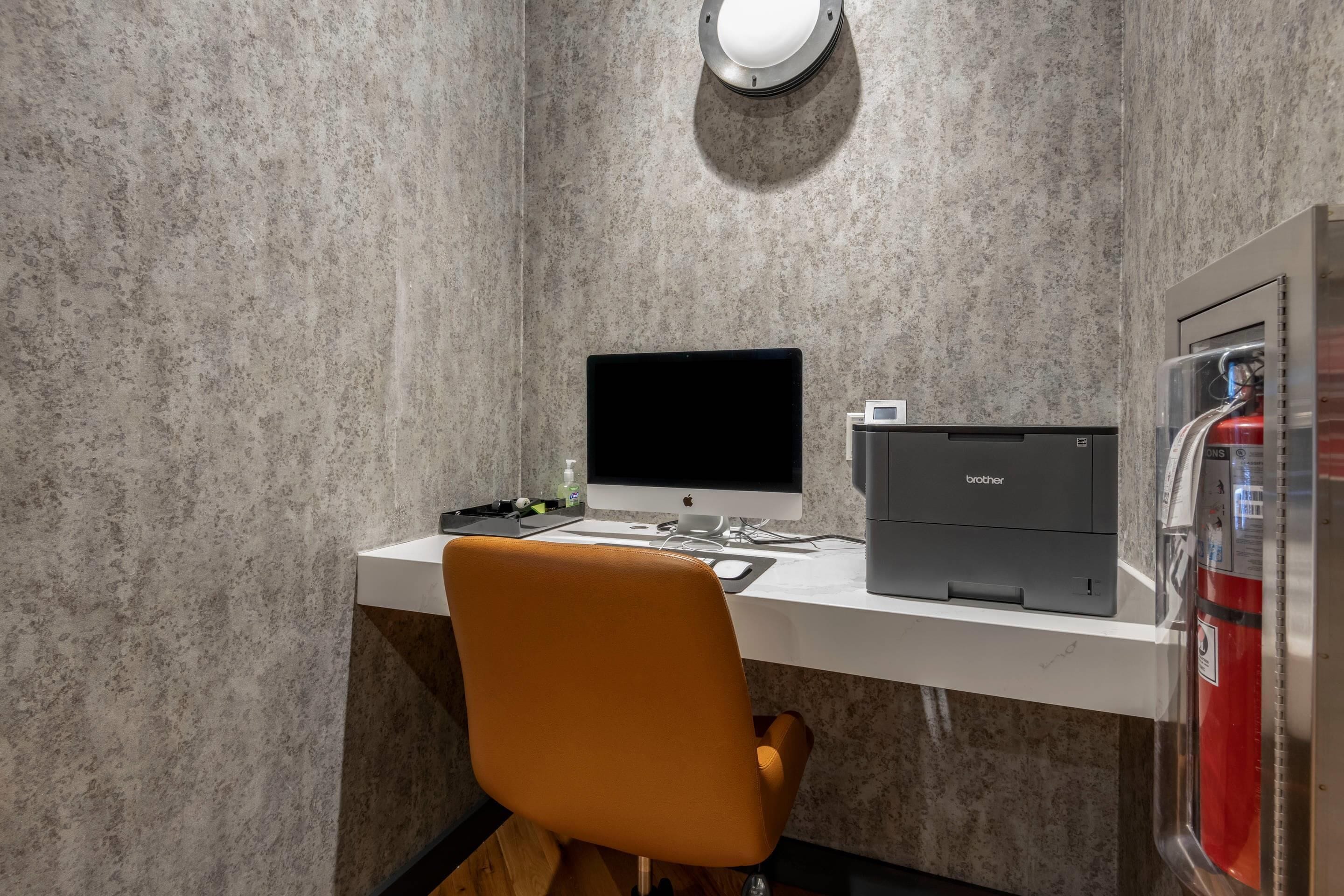 A modern office space with a white desk, an orange chair, a desktop computer, and a Brother printer.