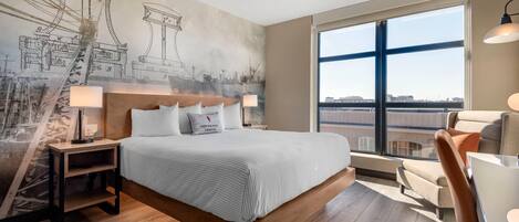 A modern hotel room with a large bed, a desk, and a chair. The room has a large window with a view of the city.