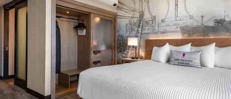 Habitación de hotel con una cama grande, un vestidor, un mural en la pared y una mesita de noche con lámpara.
