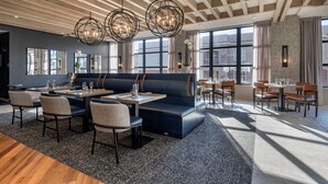 Un área de comedor moderna con un banco tapizado en azul oscuro, vigas de techo de madera y amplios ventanales que permiten la entrada de luz natural.