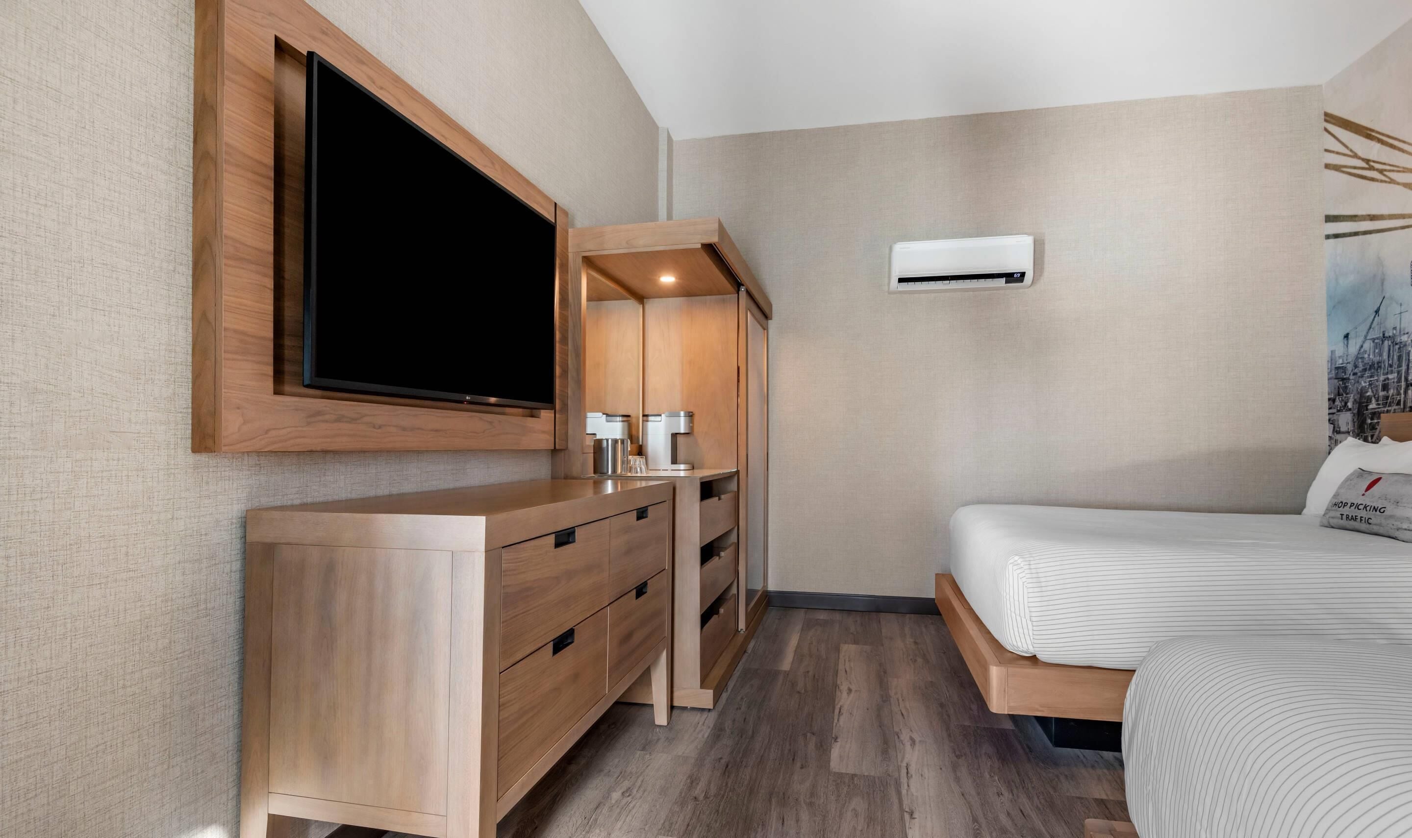 Habitación de hotel moderna con cómoda de madera, televisor de pantalla plana, máquina de café y cama con ropa de cama a rayas.