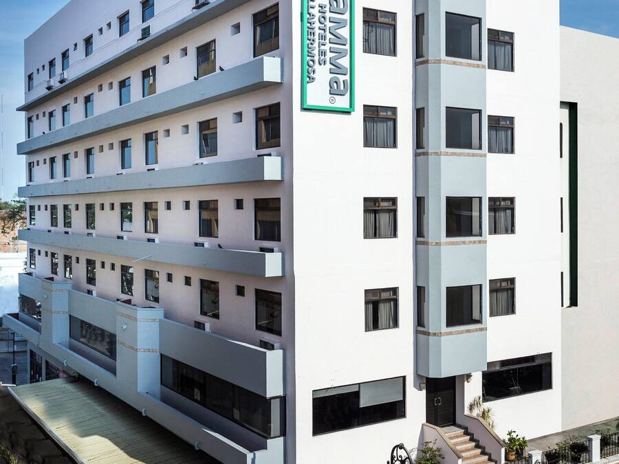 A multi-story hotel with a prominent green and white sign, multiple balconies, and a covered entrance area.