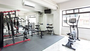 Ein Fitnessraum mit Trainingsgeräten, einem Fernseher und einem Fenster mit Blick auf Gebäude.