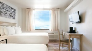 Ein Hotelzimmer mit zwei Betten, einem Schreibtisch mit Stuhl, einem Flachbildfernseher und einem Fenster mit Vorhängen.