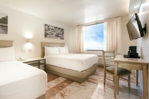 Ein Hotelzimmer mit einem großen Bett, einem Schreibtisch mit Stuhl, einem Fernseher und einem Fenster mit Vorhängen.
