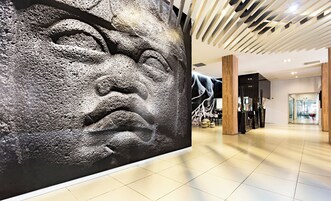 A modern interior with a large textured wall art, a wooden reception desk, and a tiled floor.